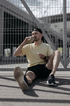 一位穿着黄衬衫的英俊年轻人在户外喝酒，散发着运动时尚的气息