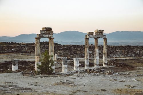 Free Atmospheric view of ancient Roman ruins with mountains in Pamukkale, Turkey at sunset. Stock Photo