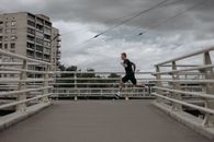 一名男子在城市桥上跑步，多云的天空下，展现了积极的生活方式