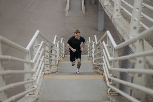 Free A tattooed man running up concrete stairs in an urban area, emphasizing fitness and motion. Stock Photo