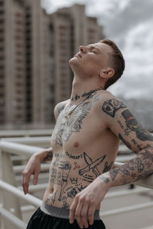 Free Shirtless man with tattoos leaning outdoors enjoying a moment of relaxation. Stock Photo