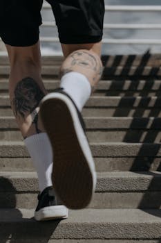 特写镜头捕捉了穿着黑色运动鞋、爬楼梯的纹身腿，展现了运动与健身的状态