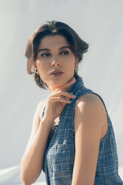 Adult thoughtful female with trendy hairstyle and eyeshadow looking away on gray background