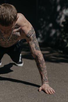 A fit, tattooed man doing push-ups on a pavement outdoors, showcasing athleticism and body art.