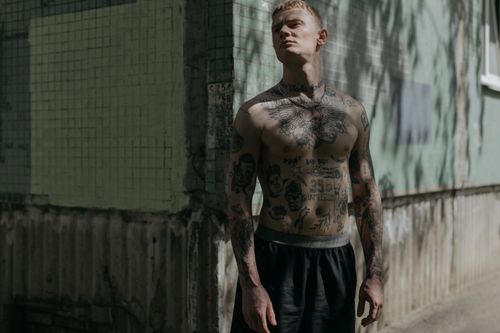 Free Sporty tattooed man standing shirtless by a concrete wall, exuding confidence and urban style. Stock Photo