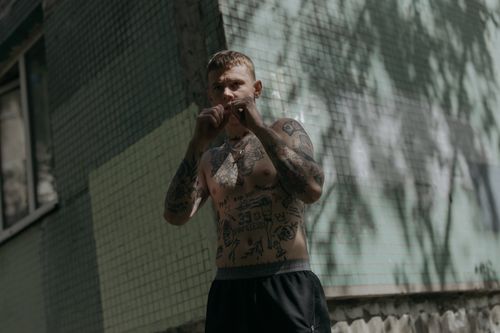 Free Tattooed man practicing boxing stances outdoors against a tiled wall, showcasing athleticism and determination. Stock Photo