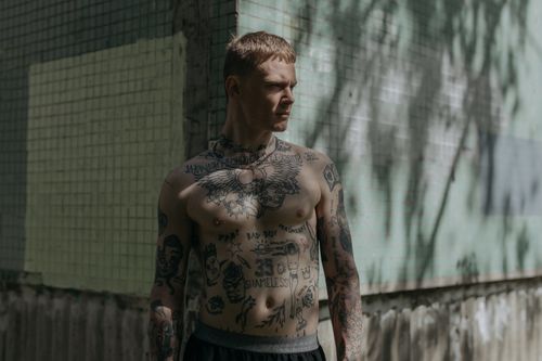 Free Shirtless tattooed man stands by textured wall, captured in daylight. Stock Photo