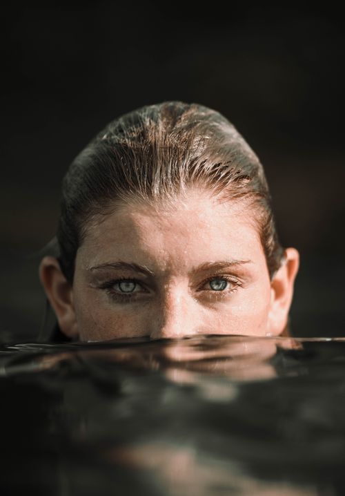 Free Young calm female traveler with wet hair and blue eyes submerging half of face into sea water and looking at camera Stock Photo
