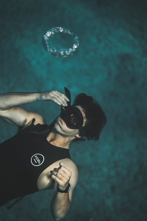 From above of anonymous young male in wetsuit and snorkeling mask submerging into water while preparing for diving