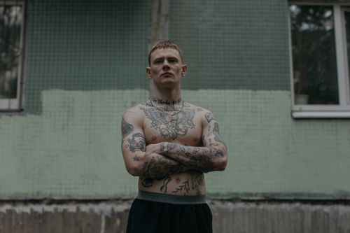 Free Shirtless tattooed man stands confidently with crossed arms against a gritty urban backdrop. Stock Photo