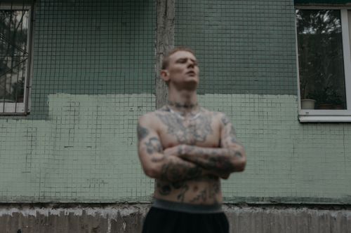 Free Shirtless tattooed man standing confidently by a greenish concrete wall. Stock Photo
