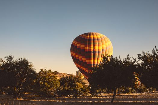 A vibrant hot air balloon floats over a serene countryside field during a sunny day.