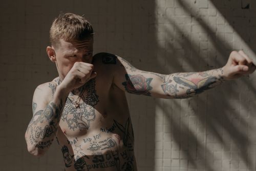 Free Tattooed boxer demonstrating a fighting stance with dramatic lighting indoors. Stock Photo
