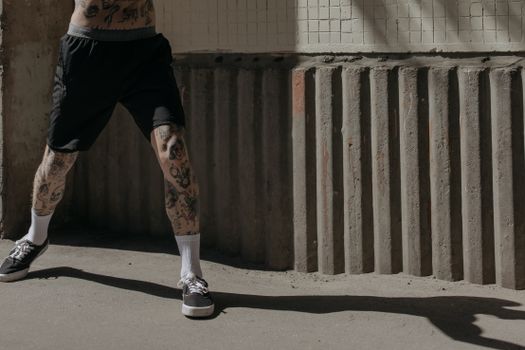 一名纹身、穿短裤的男运动员靠在混凝土墙上，站在阳光下