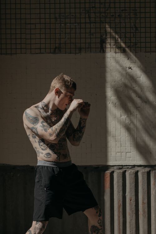 Free Tattooed man practicing boxing moves indoors in a gritty gym setting. Stock Photo