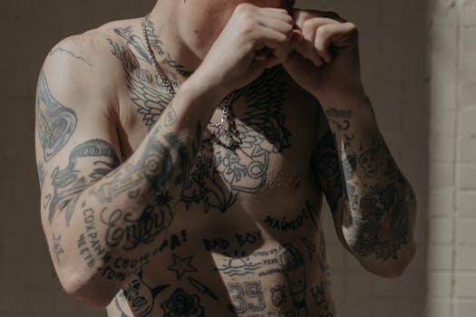A tattooed male boxer preparing for a fight, posing shirtless indoors.