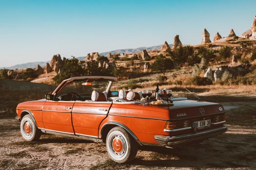 Red Mercedes-Benz convertible parked outdoors in Cappadocia with wine setup, capturing a vintage travel vibe.
