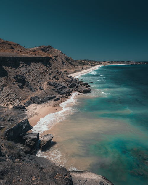 Brown Rocky Mountain Beside Blue Sea Under Blue Sky