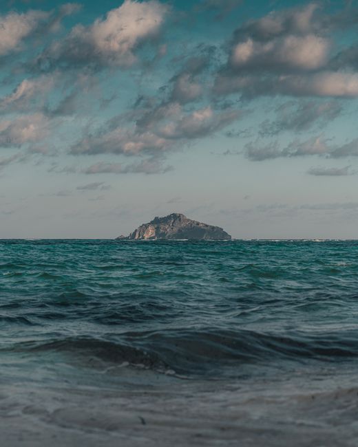 A scenic view of a distant island surrounded by vibrant blue ocean under partly cloudy skies.