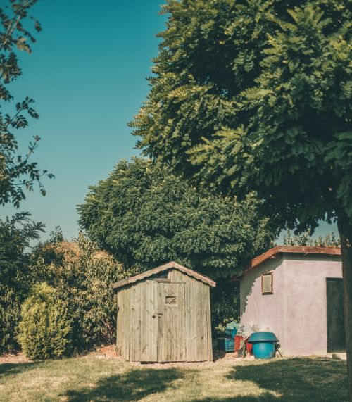 Free Charming wooden garden shed amidst lush greenery under a clear summer sky. Stock Photo