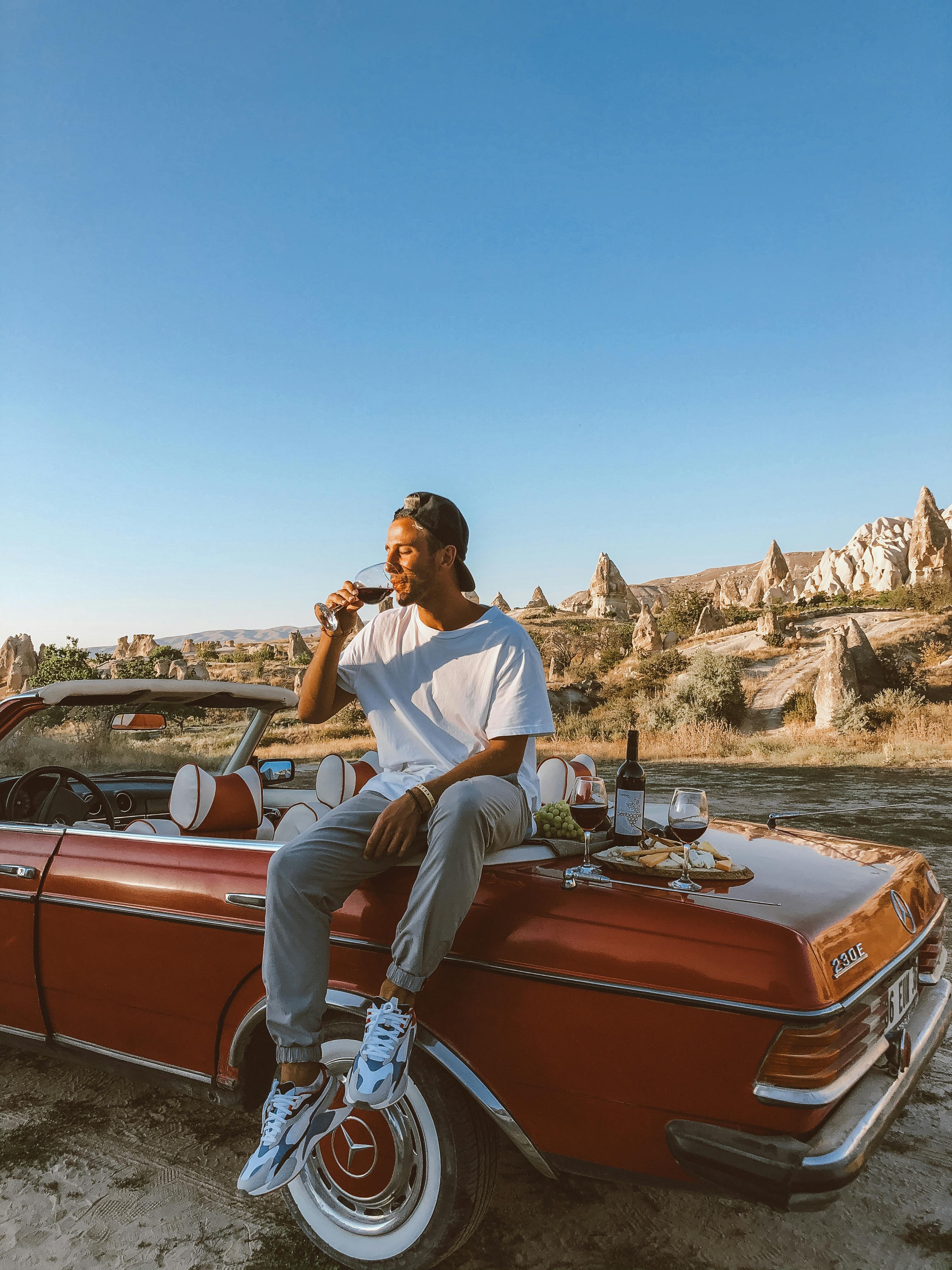 man sitting on a trunk of a vintage mercedes and drinking wine