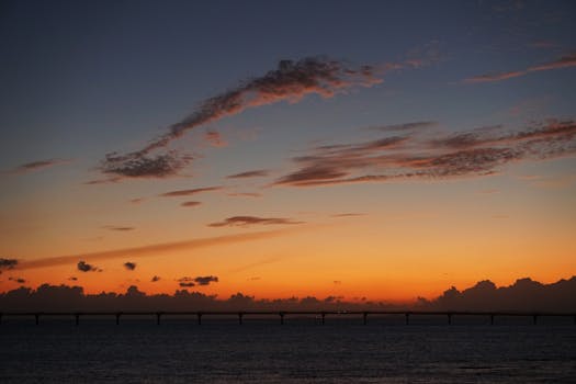 A stunning orange and blue sunset over a bridge with clouds in the sky.