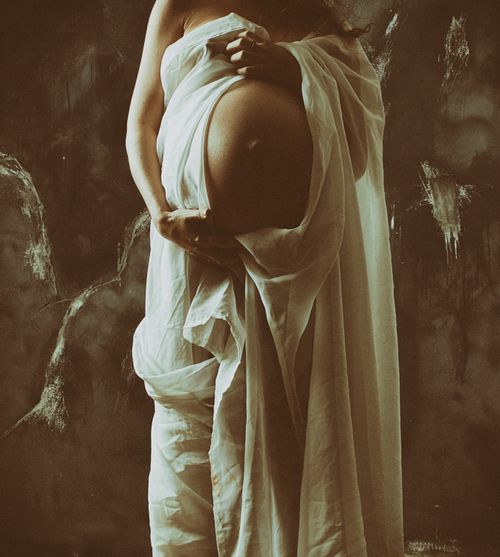Free Artistic sepia-toned portrait of a pregnant woman draped in fabric, capturing the beauty of pregnancy. Stock Photo