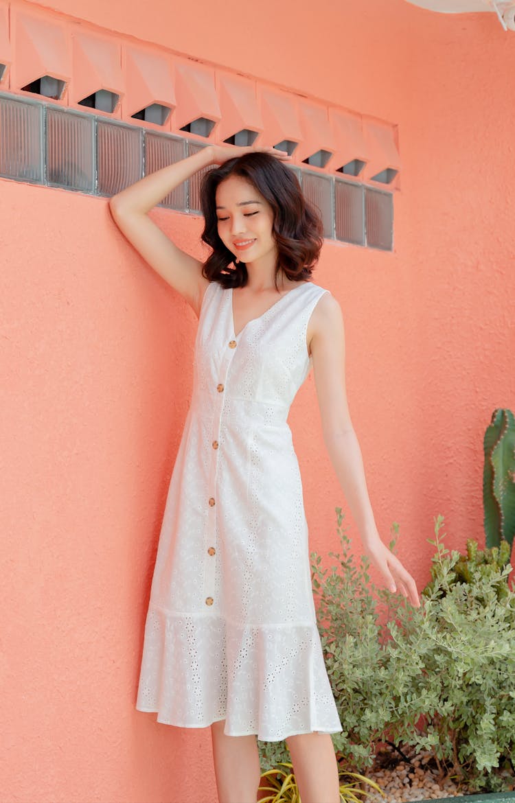 Stylish Young Asian Woman Touching Head While Standing Near Pink Wall