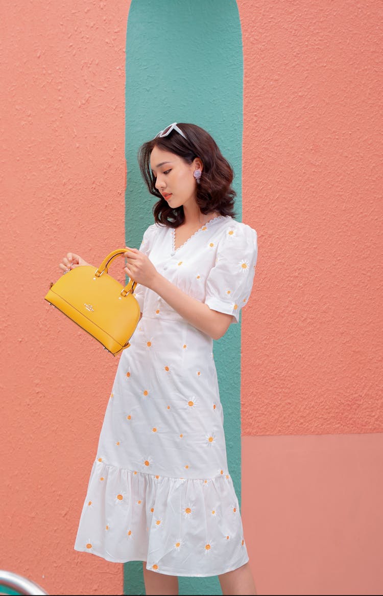 Graceful Young Asian Woman Standing Near Bright Wall With Stylish Bag In Hand