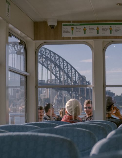 Free Travelers enjoying Sydney Harbour Bridge view through ferry windows on a sunny day. Stock Photo