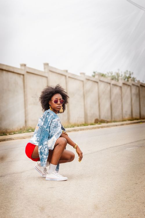 Free Afro-haired woman posing on a street, showcasing modern fashion with sunglasses and denim jacket. Stock Photo