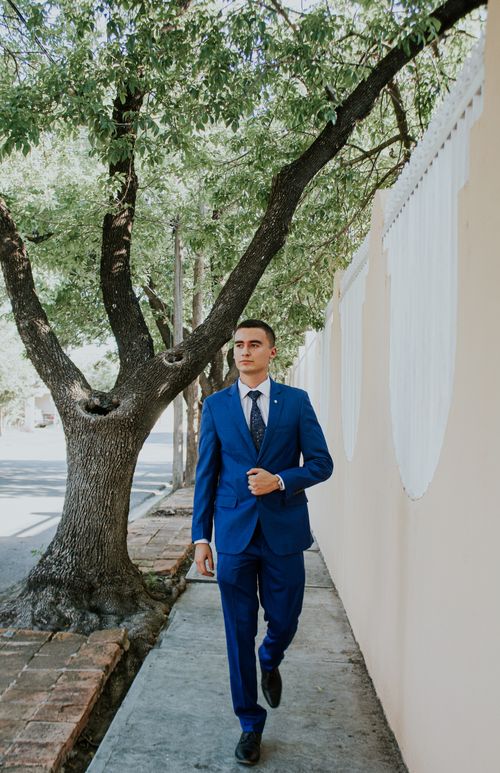 Free A stylish young man walks on a tree-lined sidewalk in a blue suit, showcasing urban fashion. Stock Photo