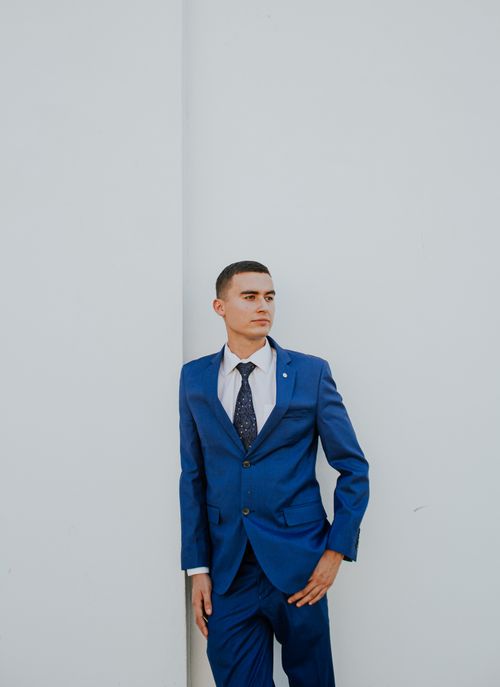 Free A stylish man in a tailored blue suit leans against a white wall, exuding confidence. Stock Photo