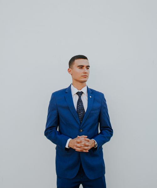 Free Portrait of a professional man in a blue suit with hands clasped. Business attire in studio setting. Stock Photo