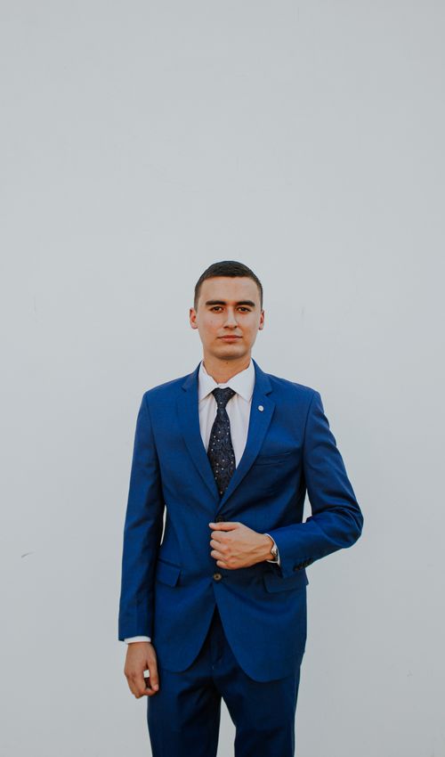 Free A confident man in a stylish blue suit poses against a plain background, exuding elegance and professionalism. Stock Photo