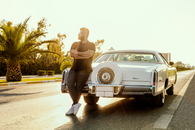 A Man in Black Shirt Leaning on a White Luxury Car Parked on the Road