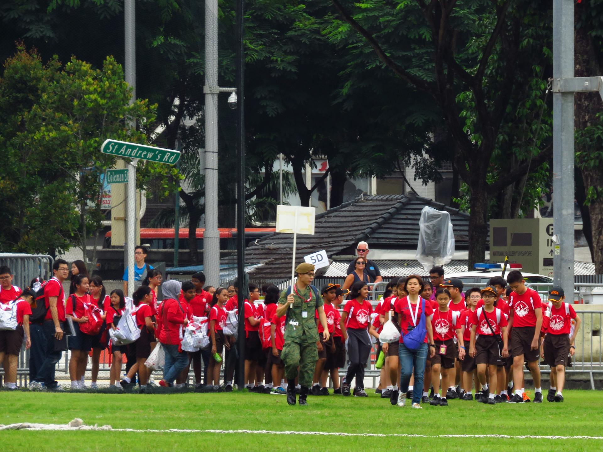 A group of children in red shirts on a guided outdoor excursion in an urban park.