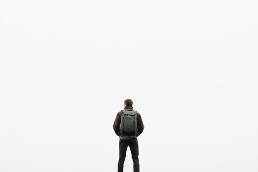 一名男子背着背包，独自站在一片空白的白色背景前