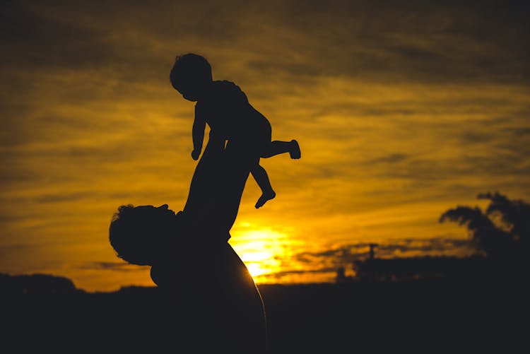 Silhouette Of Man Lifting A Baby At Sunset