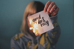 Unrecognizable female showing burning paper with written inscription and bright flame on blurred background