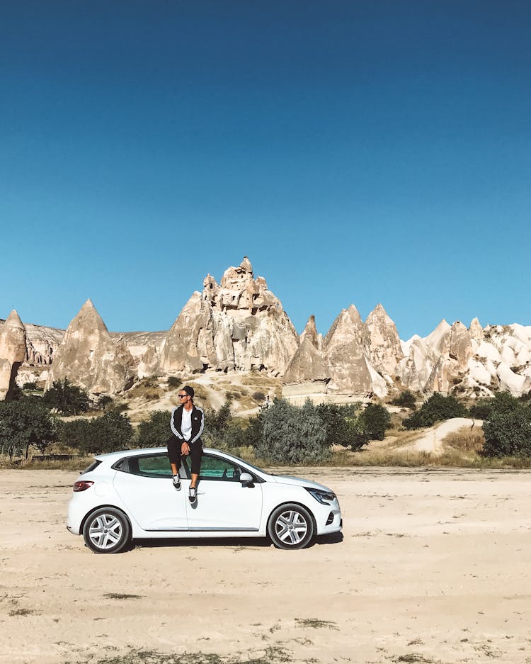 Man Sitting On A Car Near The Rock Formations