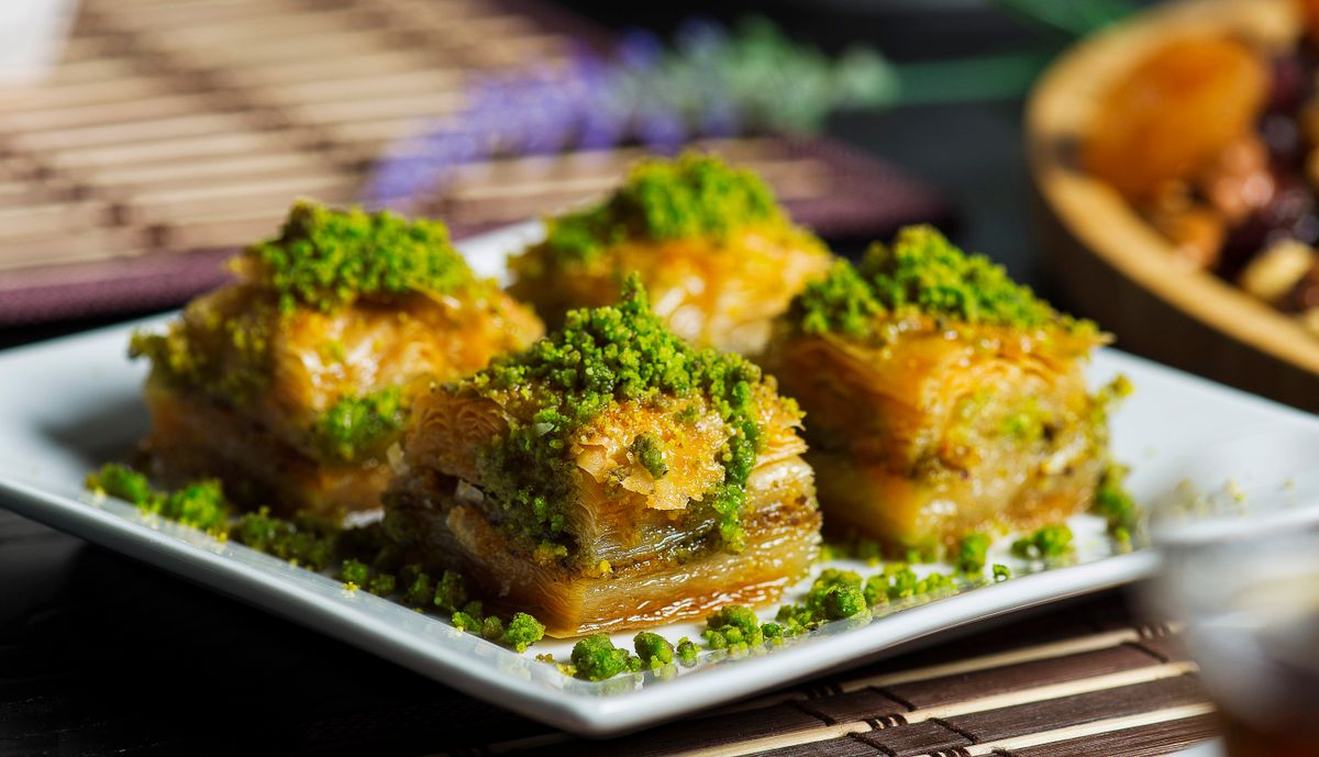 Four square baklava pieces heaped with finely ground bright green pistachios on a white plate