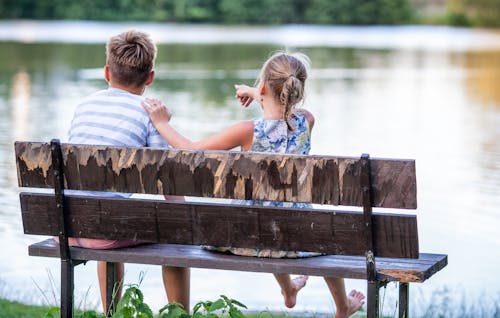 Selective Focus Photography of Boy and Girl Sitting on Bench Near Lake