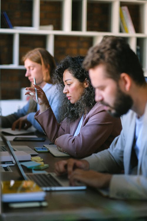 Group of young concentrated coworkers in formal wear sitting at desk and working on projects on netbooks in light office