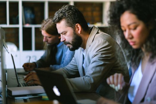 Focused young coworkers wearing formal clothes working on project on netbooks while sitting at desk in contemporary workplace