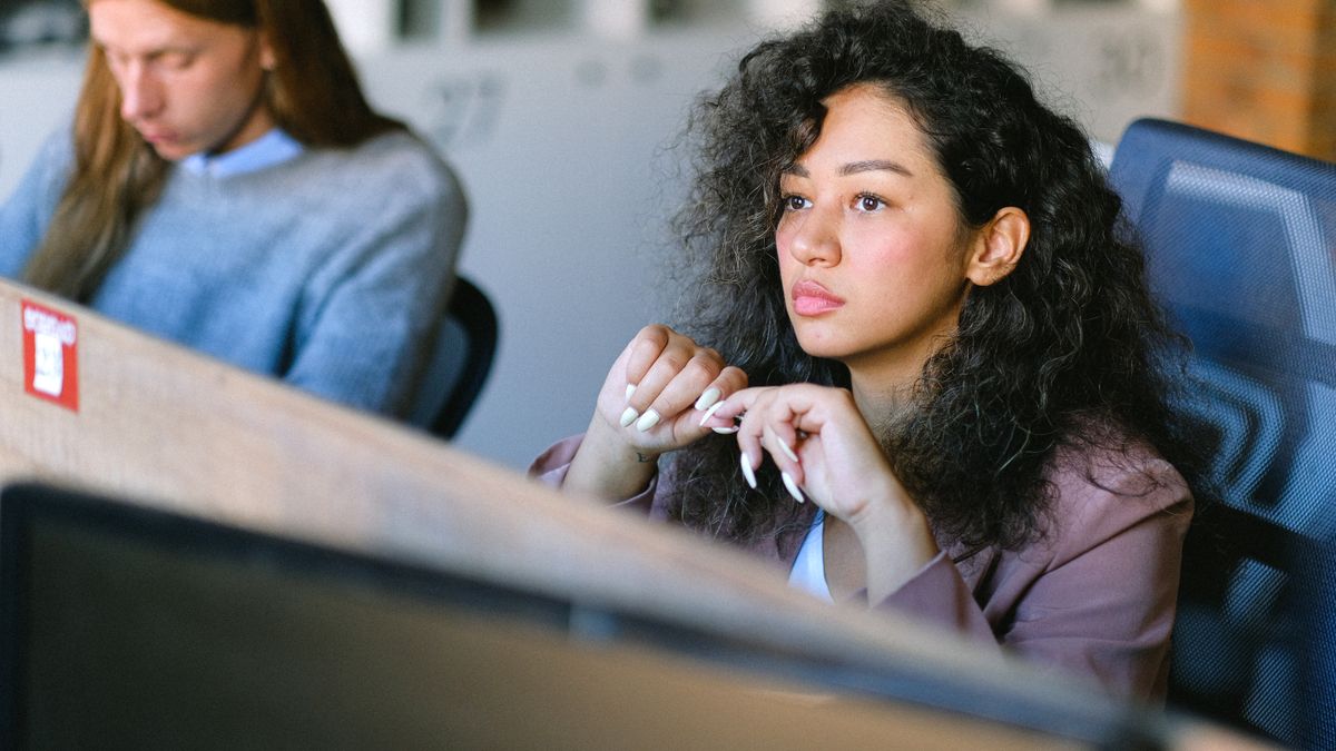 オフィスの席で手を組み、思いつめた表情で視線を外している人のイメージ