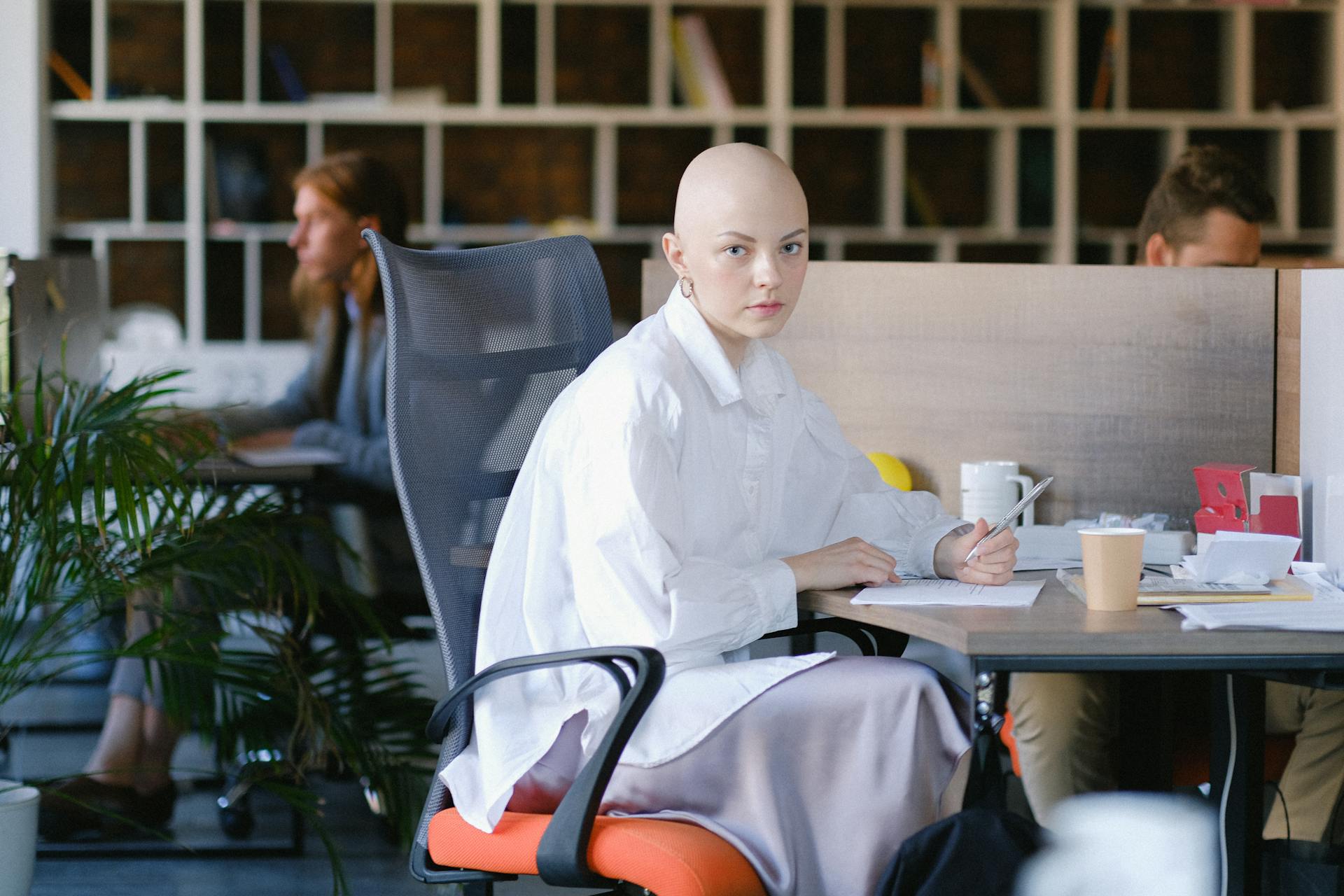 Focused bald female office employee sitting in modern open space and writing in document during work