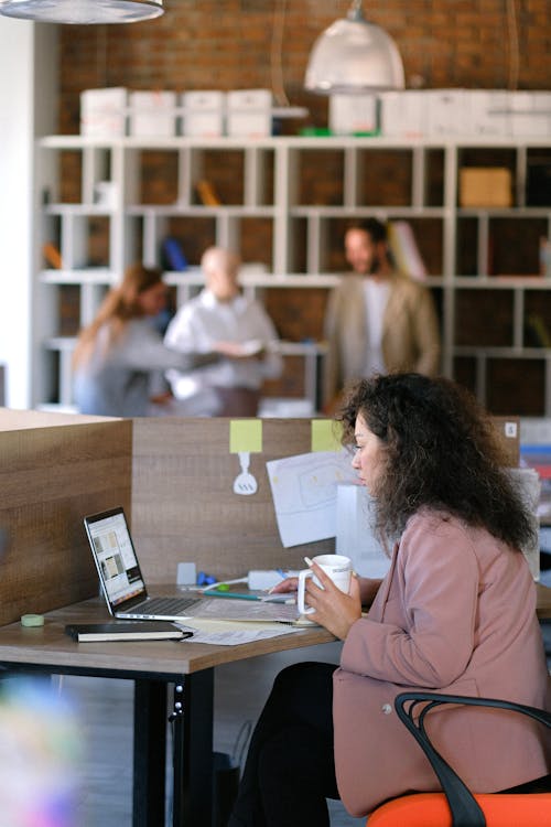 Side view of concentrated female office worker watching netbook while working in open space with colleagues discussing business