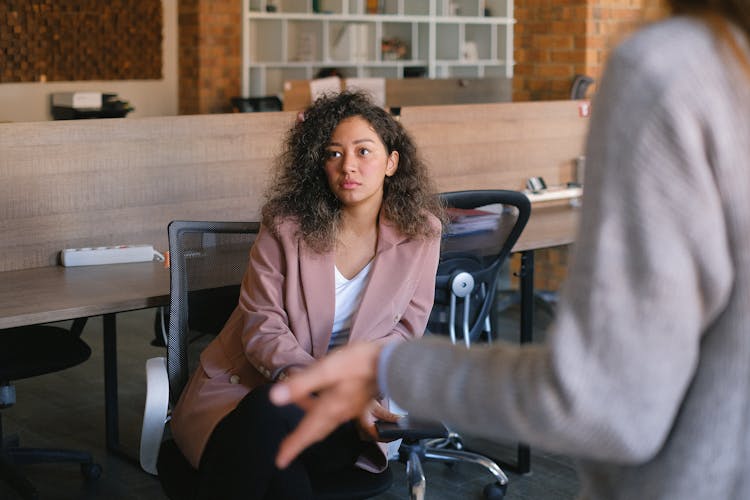 Serious Woman Listening To Colleague In Office