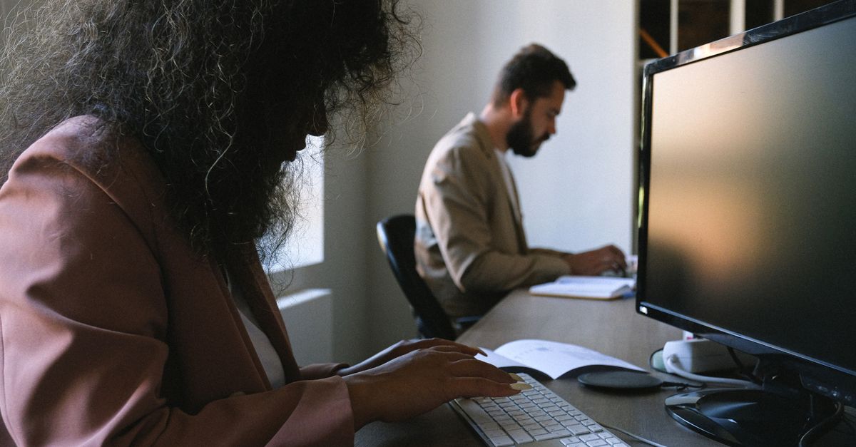 Dos profesionales concentrados en el trabajo en un entorno de oficina moderno, utilizando computadoras y cuadernos.